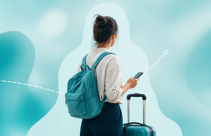 Woman traveler holding a phone beside a suitcase on a soft turquoise background